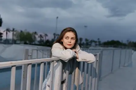 Задумчивая бизнес-леди в современном элегантном наряде опирается на перила в городской обстановке, воплощая сочетание уверенности и амбиций
