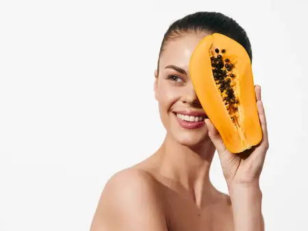 Красивая молодая женщина с маской из папайи на лице наслаждается спа-процедурой на белом фоне