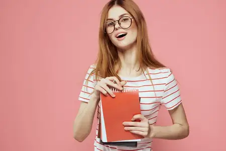 Молодая студентка с книгами на розовом фоне, в очках
