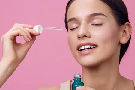 Веселая молодая женщина с безупречной кожей наносит питательную сыворотку для лица, чтобы подчеркнуть свою естественную красоту