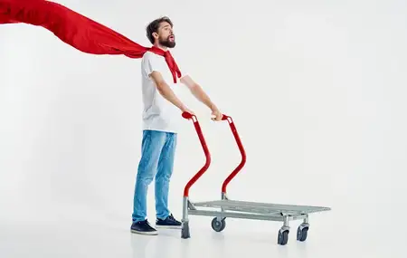 Бородатый мужчина в красном плаще держит в руке грузовую тележку