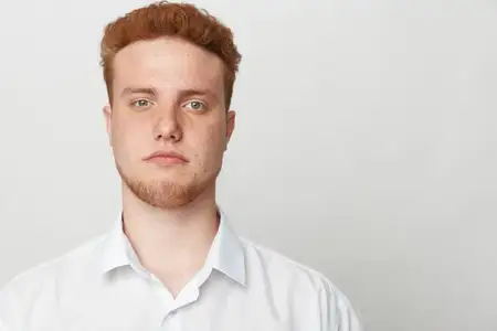 Крупный план молодого рыжеволосого мужчины с веснушками в белой рубашке, смотрящего прямо в камеру