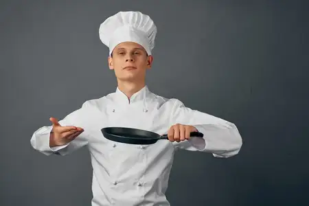Повар в форме держит в руках сковороду и готовит, работая в ресторане