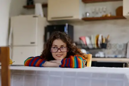 Живая женщина на домашней кухне, расслабленная и довольная, красочная одежда и очки обрамляют уютную повседневную сцену комфорта, творчества и непринуждённой жизни