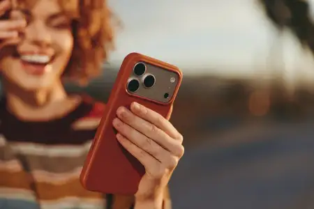 Женщина улыбается с вьющимися волосами на улице, смартфон в руке