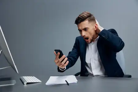 Бизнесмен с телефоном, испытывая эмоции, работает перед компьютером в офисе