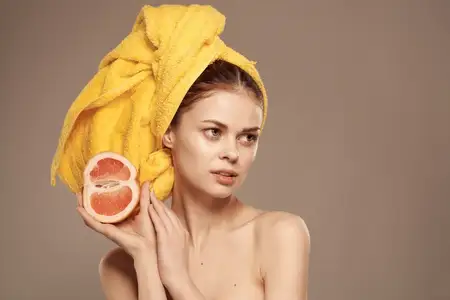Женщина с обнаженными плечами, желтым полотенцем на голове и грейпфрутом в руках