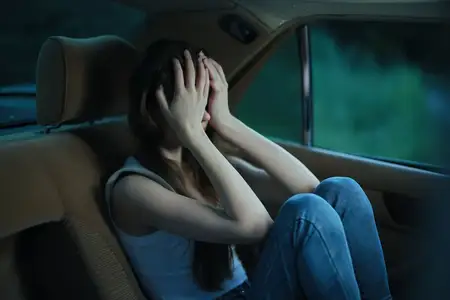 Молодая женщина сидит в машине, выражая глубокие чувства печали и отчаяния, закрывая лицо руками