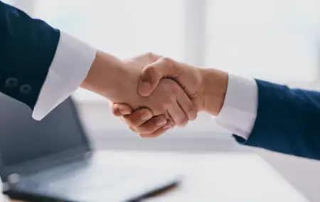 Деловые люди пожимают руки на светлом фоне, рядом офисное окно и ноутбук