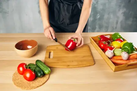 Женщина в черном фартуке на кухне нарезает овощи