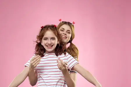 Женщина и маленькая девочка на розовом фоне веселятся: сёстры, подруги, семья
