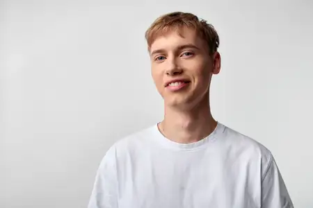 Непринужденная поза улыбающегося мужчины в белой футболке на ярком студийном фоне передает доступную энергию