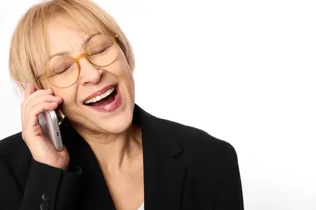Улыбающаяся женщина в очках прижимает смартфон к уху, деловая одежда, мягкий студийный свет, крупный план портрета