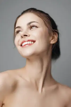 Молодая женщина улыбается и смотрит вверх, на небо, на сером фоне