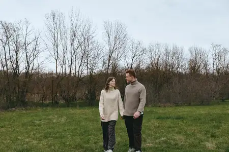 Влюблённые прогуливаются по открытому лугу, тёплые свитера, повседневный стиль, мирный пейзаж, приглушённые тона, свежий воздух, искренний момент, близость и дружба, образ жизни на свежем воздухе…
