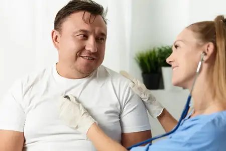Женщина-врач проводит осмотр пациента-мужчины с помощью стетоскопа