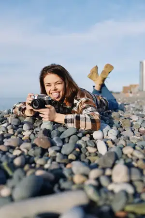 Непринужденная женщина-фотограф на галечном берегу лежит, чтобы снимать ручной камерой