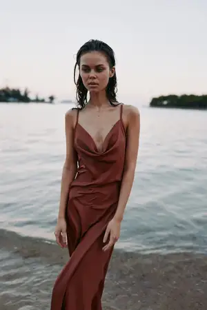 Кинематографичная outdoor-сцена у воды, сочетающая элегантность и созерцательность с естественным бризом, приглушенной палитрой и безмятежной прибрежной атмосферой