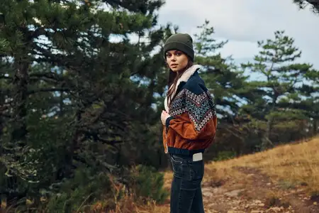 Женщина в модной шляпе и куртке наслаждается природой на тихом холме, окружённом деревьями