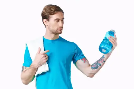 Спортивный парень в синей футболке с бутылкой воды стоит в реке