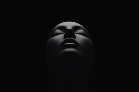 Минималистичный портрет вызывает ощущение тайны, тишины и самоанализа, поскольку освещение изолирует черты лица и подчеркивает текстуру, форму и настроение в студийной обстановке
