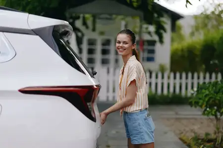 Улыбающаяся молодая женщина стоит рядом с белым автомобилем, создавая живую и позитивную атмосферу