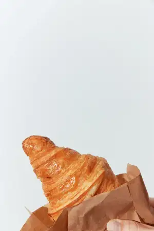 Мужчина держит круассан, проложив между рукой и выпечкой кусочек коричневой бумаги