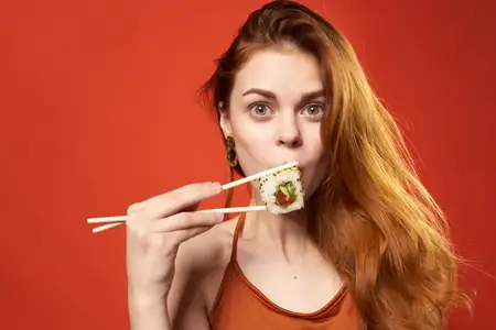 Симпатичная рыжеволосая женщина с суши, палочками для еды, диета, еда, красный фон