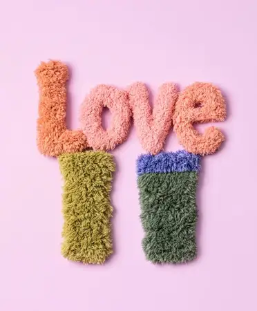 Игривая и красочная типографика слова «Love», выполненная из мягких текстур, идеально подходит для декора, поделок или сезонных праздников, на светло-розовом фоне