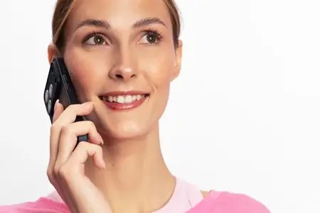 Молодая женщина с сияющими глазами улыбается, прижимая смартфон к уху