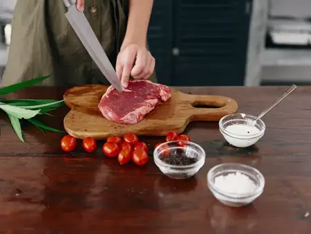 Женщина с ножом в руке нарезает стейк для жарки на кухне
