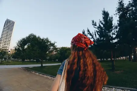 Женщина в стиле лайфстайл в современном бохо-вестерн деним стрит-стайле идёт через зелёный городской парк с высокими зданиями на заднем плане, с плёночными тонами и расслабленным настроением