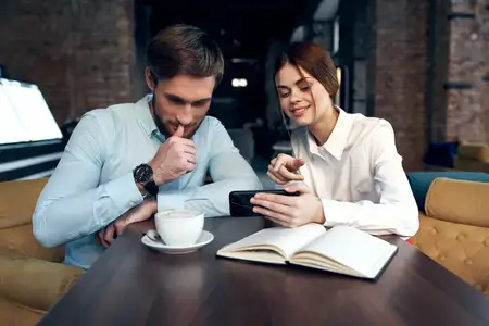 Мужчина и женщина, офисные работники, сидят в кафе, перекусывают, отдыхают, общаются, в руках телефоны