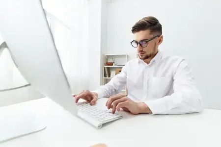Бизнесмен в белой рубашке сидит за компьютером с телефоном в офисе