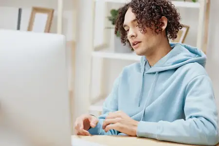 Портрет мужчины в синей куртке на фоне компьютера с телефоном
