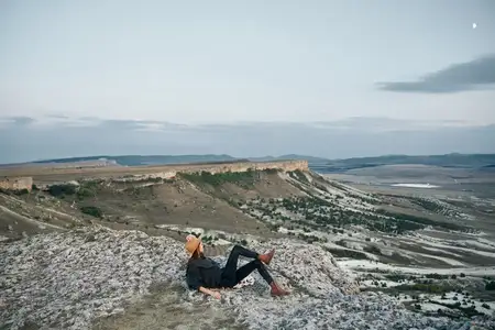 Безмятежная женщина на закате созерцает долину и горы, сидя на камне