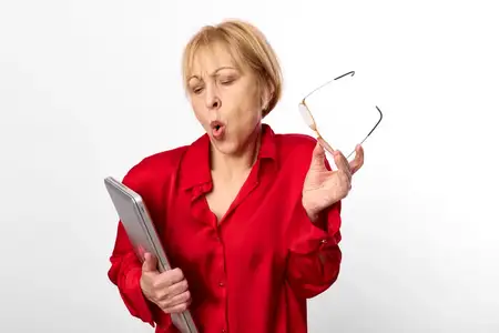 Пожилая женщина, удивлённая, держит очки, смартфон и планшет