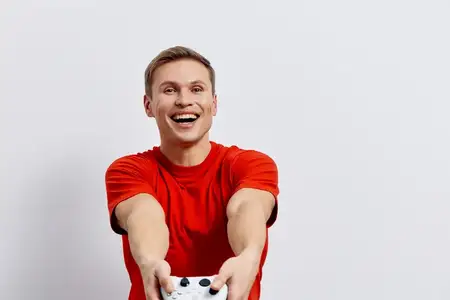 Веселый мужчина в ярко-красной футболке активно наслаждается игрой с игровым контроллером в руках, широко улыбается, позитивное настроение, простой фон, студийный снимок, яркая цветовая палитра