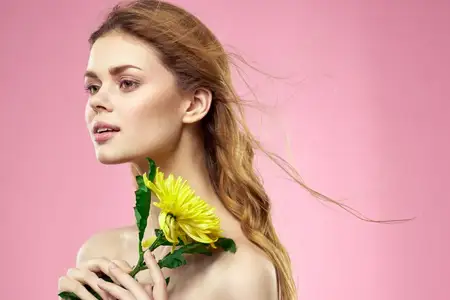 Красивая девушка с жёлтым цветком на розовом фоне, обнажённые плечи, макияж