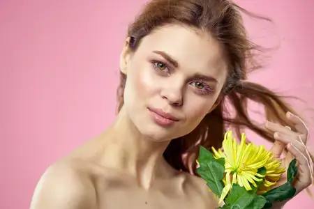 Красивая женщина с обнажёнными плечами и жёлтым цветком в руках на розовом фоне