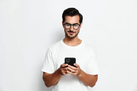 Веселый молодой человек в очках проверяет смартфон в руках, демонстрируя современные технологии и связь