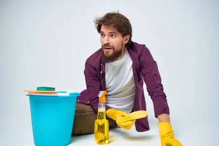 Мужчина с моющим средством убирает квартиру, выполняя рутинную работу