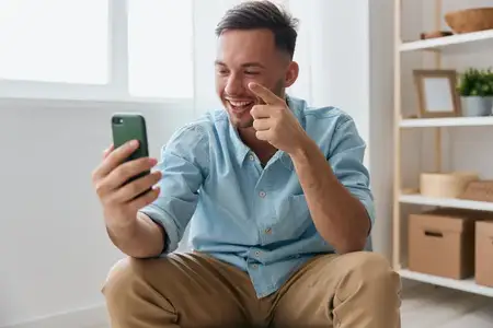 Весёлый, улыбчивый, общительный парень разговаривает с семьёй по видеозвонку, обсуждает последние приятные новости, поднимает палец вверх и смотрит на экран