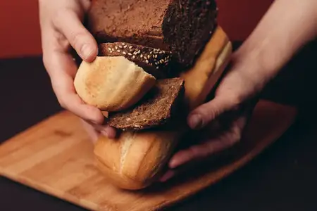 На деревянной доске на красном фоне лежат нарезанный багет и буханка ржаного хлеба