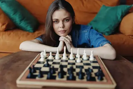 Молодая женщина играет в шахматы, сидя на диване дома