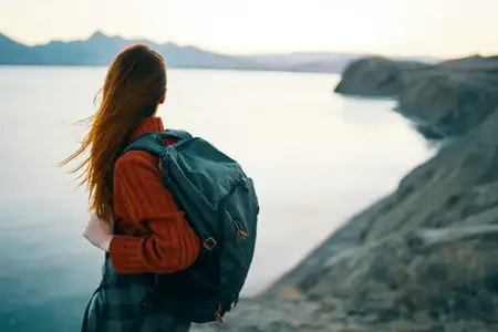 Женщина в красном свитере с рюкзаком на фоне моря и гор