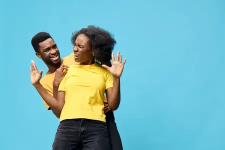 Счастливая пара весело проводит время вместе в стильных желтых рубашках, подчеркивая игривость и нежность на ярком синем фоне, запечатлевая радостные моменты