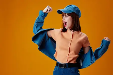 Портрет очаровательной девушки в кепке и джинсовой куртке на жёлтом фоне