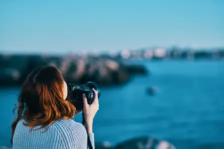 Женщина фотографирует море в горах, вид со спины