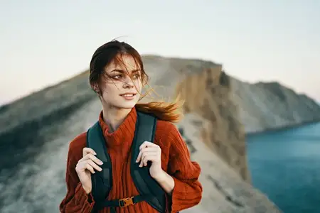 Природа, горы, свежий воздух — молодой путешественник с рюкзаком и в свитере отдыхает у моря